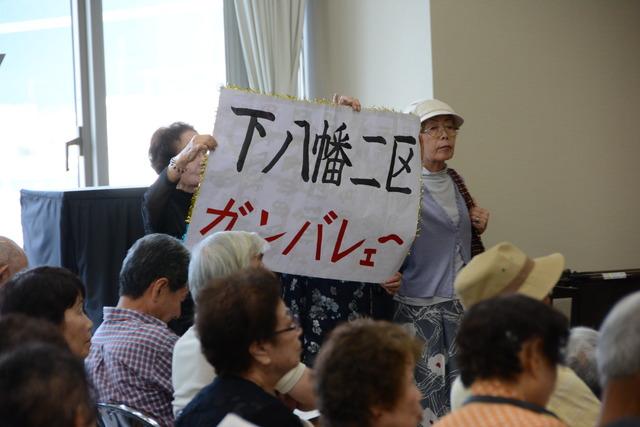 カラオケ大会 「下八幡2区 ガンバレェー」の応援の紙を持っている写真