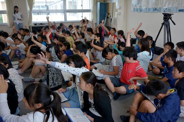 教室の床に座って手を挙げている竜王小の児童たちの写真