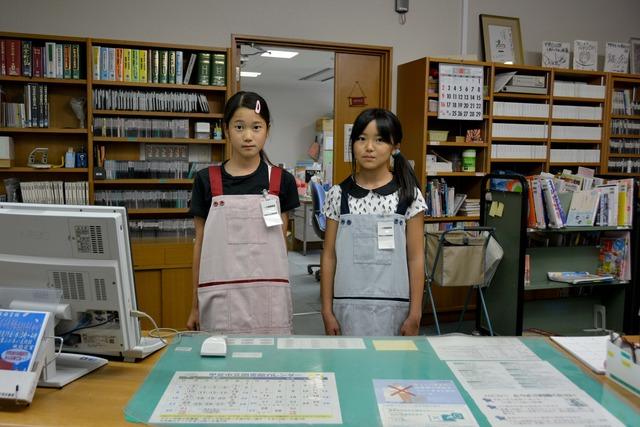 2人の女の子がエプロンを付けて図書館のカウンターに立っている写真