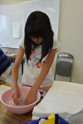 女の子が洗面器の水の中で紙やすりを使っている写真