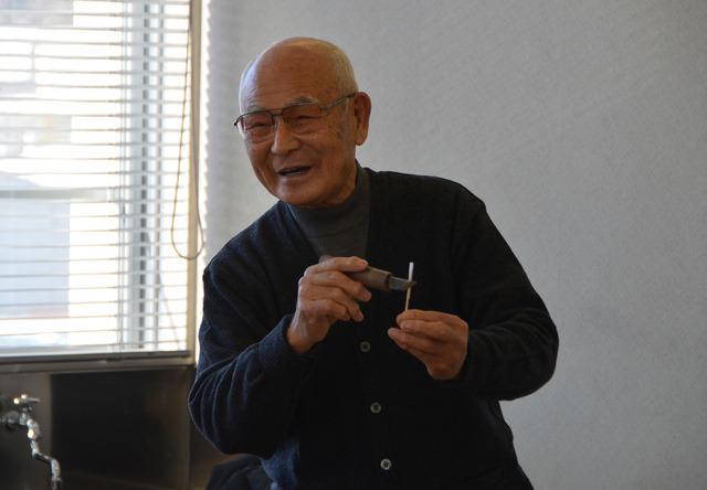 小さな刀と竹の棒を持ちながら話をしている講師の写真