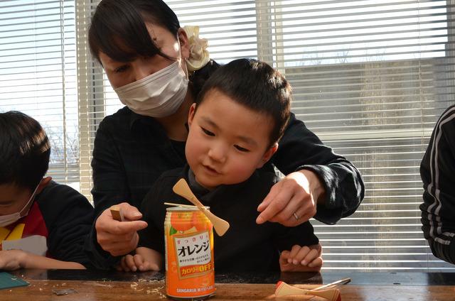 缶の上に竹とんぼをのせて見ている親子の写真