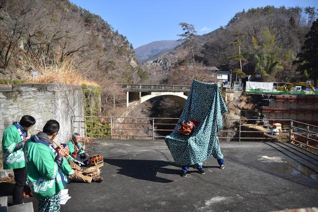 緑の法被を着た男性が演奏する横笛や太鼓に合わせて獅子舞が披露される写真