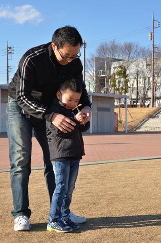 屋外で作った竹とんぼを飛ばす親子の写真