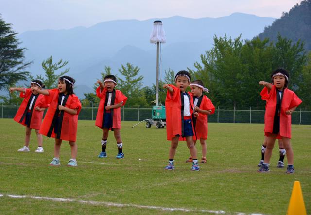 赤い法被を着た子どもたちが片手を前に突き出して踊っている写真