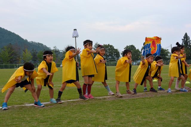 黄色の法被を着た子どもたちが片手を前に突き出して踊っている写真