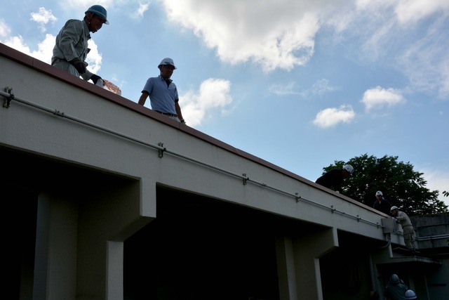 2人の作業員が建物の屋根に上って作業している写真