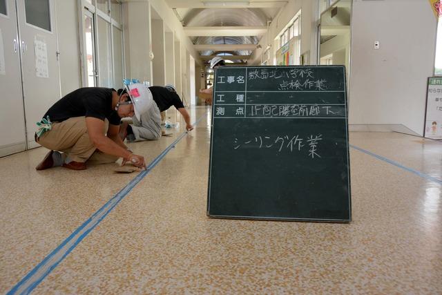 2人の作業員が校舎の廊下にシーリング材を埋める作業を行う写真
