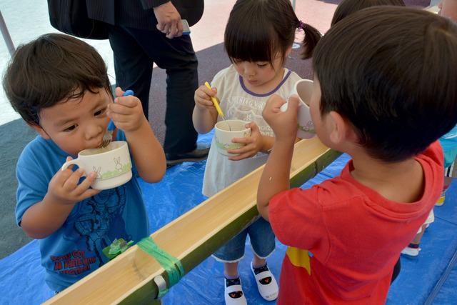 流しそうめんを食べている三人の園児の写真