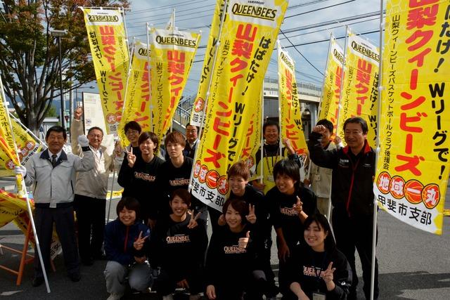 (写真)のぼり旗と一緒にピースサインやガッツポーズの選手と職員たち