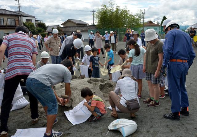 双葉中学校にて甲斐市総合防災訓練に参加されている方たちが土のう袋にスコップを使って砂を入れている写真