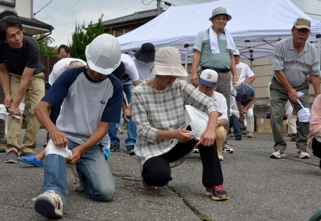 双葉中学校にて甲斐市総合防災訓練に参加されている方たちが自分の膝に三角巾をあて応急救護訓練をしている写真