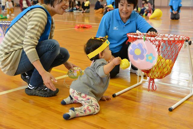 小さな女の子が黄色のボールをカゴに入れようとしている写真