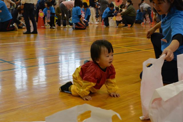 小さな男の子が袋を持った先生のもとまでハイハイで向かっている写真