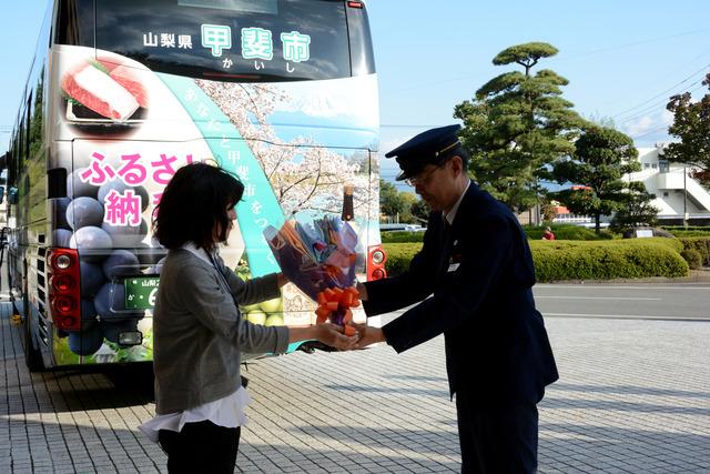 ラッピングバスの前で市職員からドライバーへ花束を贈っている写真