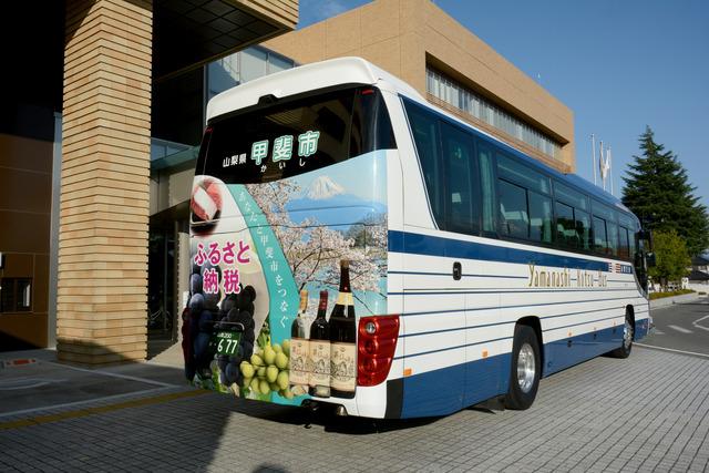 背面に「甲斐市」とふるさと納税の返礼品や富士山がデザインされたラッピングバスの写真
