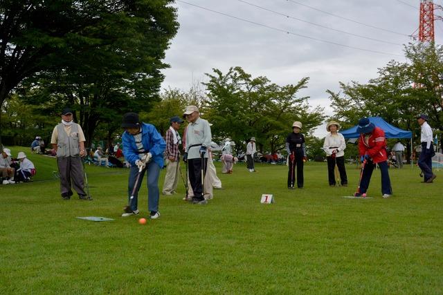小雨まじりの中グラウンドゴルフを楽しむ参加者の写真