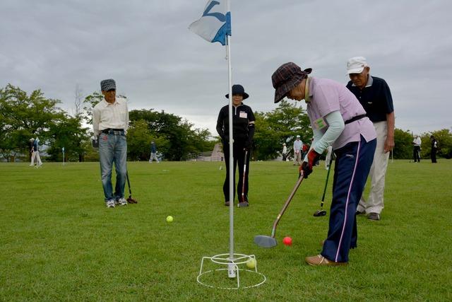 ほかの参加者が見守る中グラウンドゴルフを楽しむ女性の参加者の写真