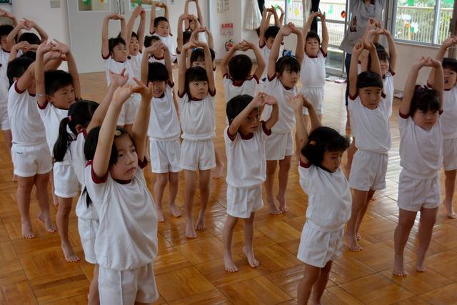 手を伸ばして頭の上で組むポーズをとる園児たちの写真