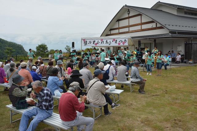 来場者と屋外ステージで吹奏楽団がコンサートを開いている写真