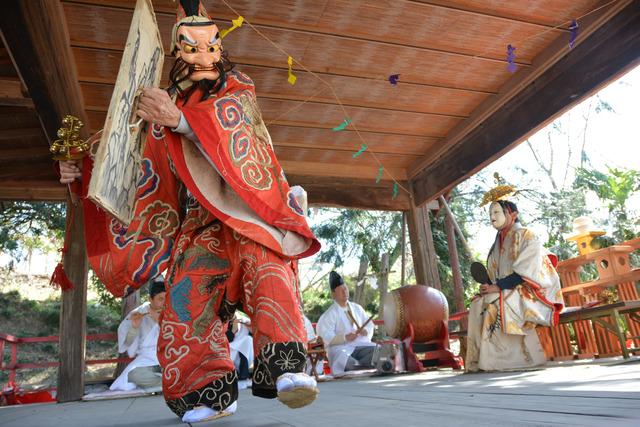 横笛と太鼓の演奏に合わせてお面を付け赤い衣装を着た男性が神楽を舞っている写真