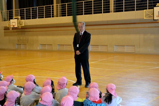 学校の体育館で、園児たちにお話をしている校長先生の写真