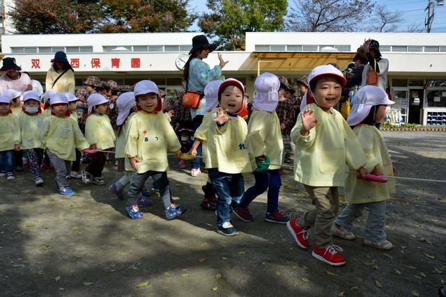 仲良く手を繋いで手を振りながら歩いている園児たちの写真