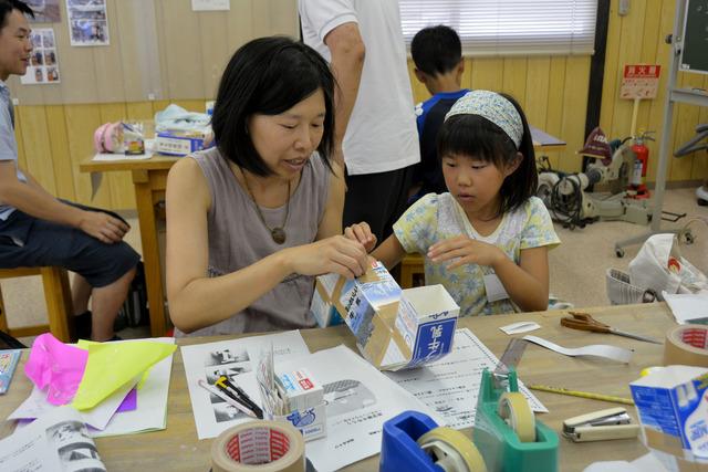 切った牛乳パックをガムテープでつなぎ合わせている女の子と女性の写真