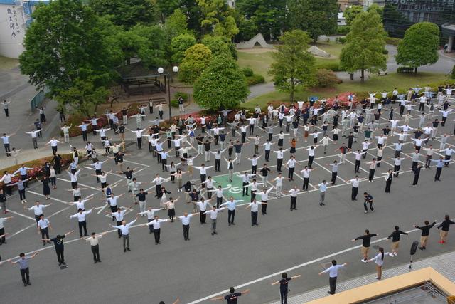 たくさんの人が広い駐車場で広がって体操をしている様子の写真