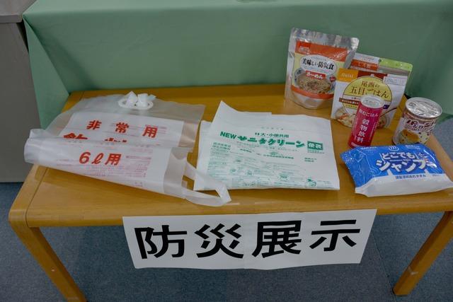 竜王図書館の防災展示コーナーに簡易トイレや非常食などの防災備蓄品が並べられている写真