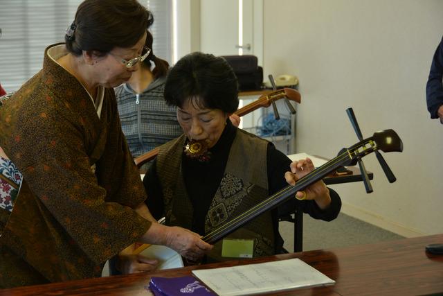 講師に教わりながら調子笛を使って三味線の音程を調整している女性の写真