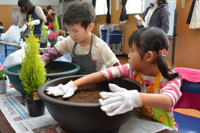 大きな鉢に土を入れ、軍手をした子ども達が地ならしをしている写真