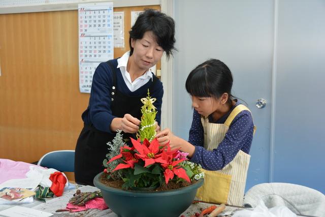 親子が鉢に植物を植え、リボンをつけている写真