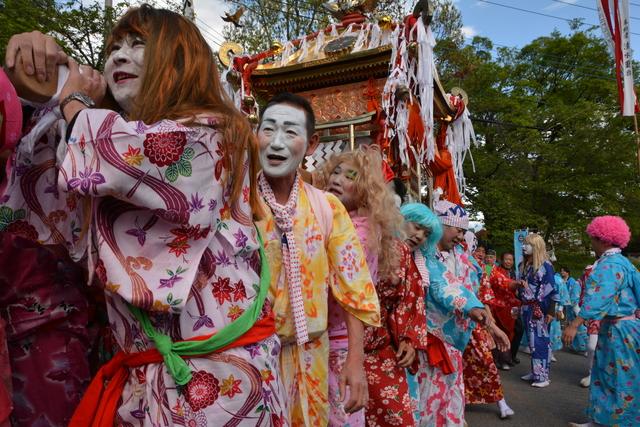 女装した男性たちが楽しそうに神興をかつぐ様子の写真