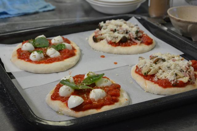 トマトソースにモッツァレラチーズやバジル等のトッピングされた、オーブンで焼く前のピッツァの写真
