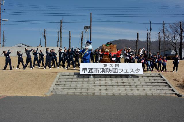 消防団の半被を着たやはたいぬと一緒にラジオ体操をする人々の写真