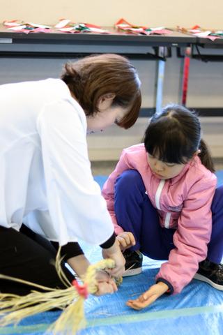 母親と女の子がしめ縄を編んでいる写真