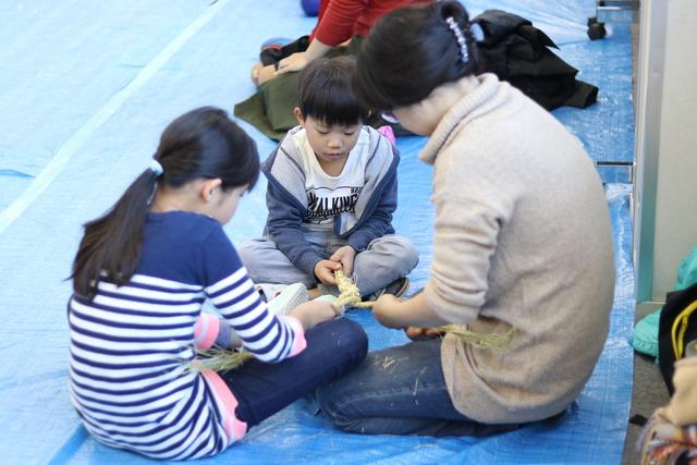母親と男の子と女の子がしめ縄を編んでいる写真
