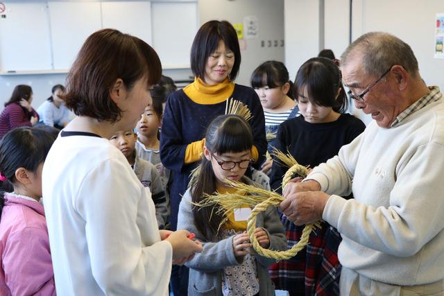 親子が集まり講師に作ったしめ縄を見てもらっている写真