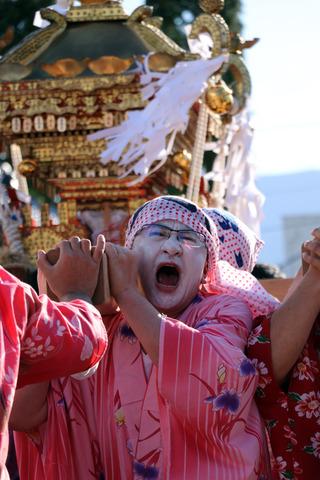 女装した男性が真剣に神興をかつぐ様子の写真