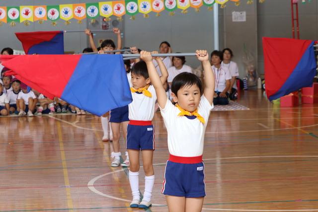青と赤の大きな旗を持った園児が演技を披露している写真