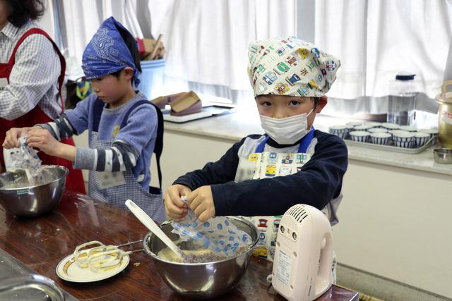 エプロン姿の男の子がケーキの生地にココアパウダーを混ぜている写真