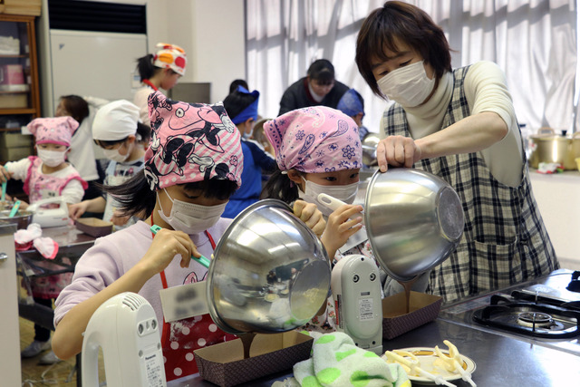 小学生が大人に手伝ってもらいながら、生地を型に流し込んでいる写真