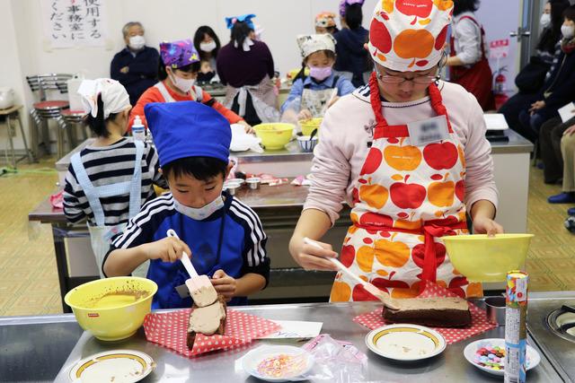 男の子と女の子が焼きあがったスポンジにチョコレートクリームを塗っている写真