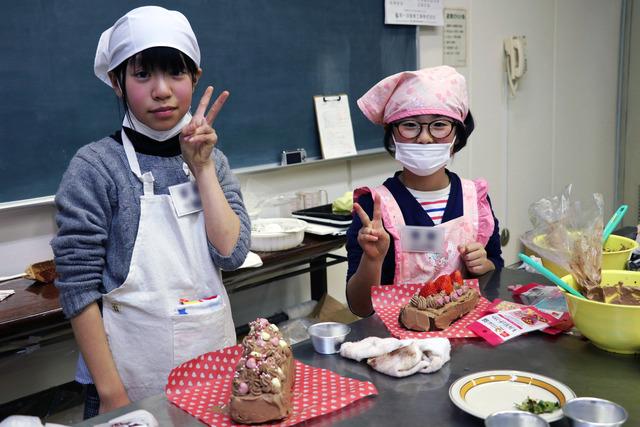 完成したケーキを前にピースサインの二人の女の子の写真