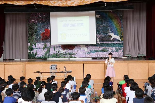 竜王西小学校の体育館にて6年生の児童たちに市選挙管理委員会職員が話をしている写真