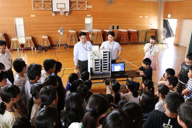 竜王西小学校の体育館にて児童たちが候補者別に仕分けられる読取分類機を見ている写真