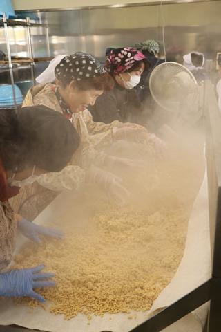 湯気が立つ大豆の前で作業する女性たちの写真