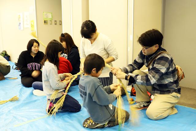 稲わらの編みこみをしているお父さんと子どもの写真