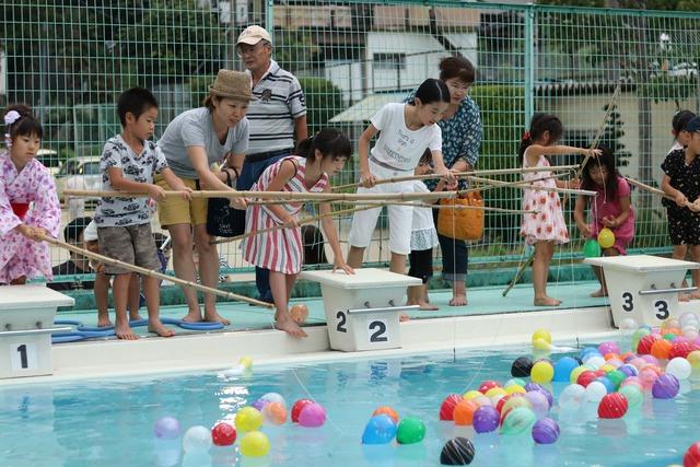 プールにたくさんのヨーヨーが浮かべられ、子ども達が竹の竿で釣っている写真